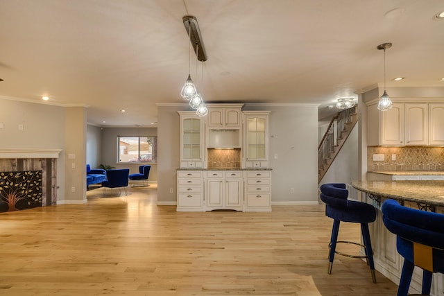 kitchen featuring ornamental molding, light wood finished floors, a fireplace, and glass insert cabinets