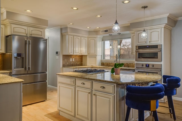 kitchen with light stone counters, cream cabinets, stainless steel appliances, visible vents, and hanging light fixtures