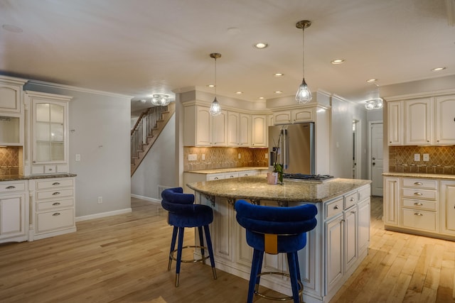 kitchen featuring light wood finished floors, high end refrigerator, a kitchen island, glass insert cabinets, and light stone counters