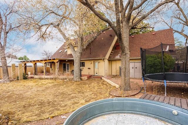 view of front of property featuring a trampoline, roof with shingles, fence, and stucco siding