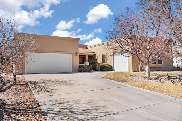 adobe home with a garage, a tile roof, driveway, and stucco siding