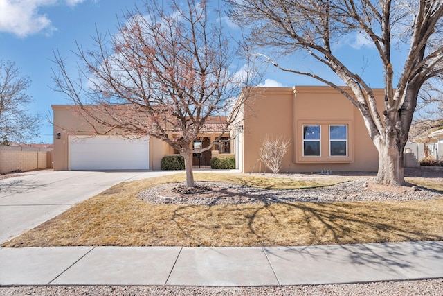 pueblo revival-style home featuring an attached garage, fence, concrete driveway, and stucco siding