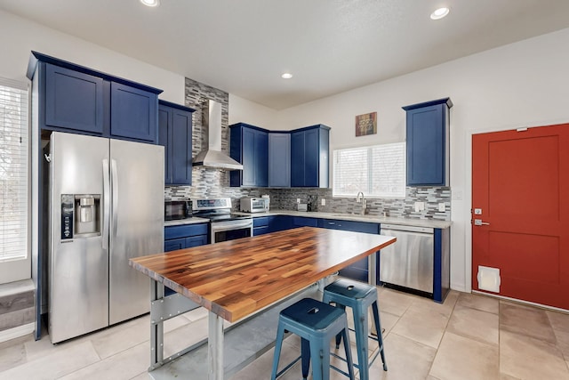 kitchen with blue cabinetry, light countertops, decorative backsplash, appliances with stainless steel finishes, and wall chimney range hood