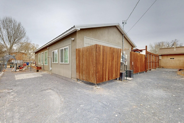 view of side of property featuring fence, cooling unit, and stucco siding