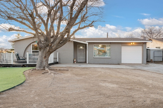 single story home featuring a deck, driveway, brick siding, and an attached garage