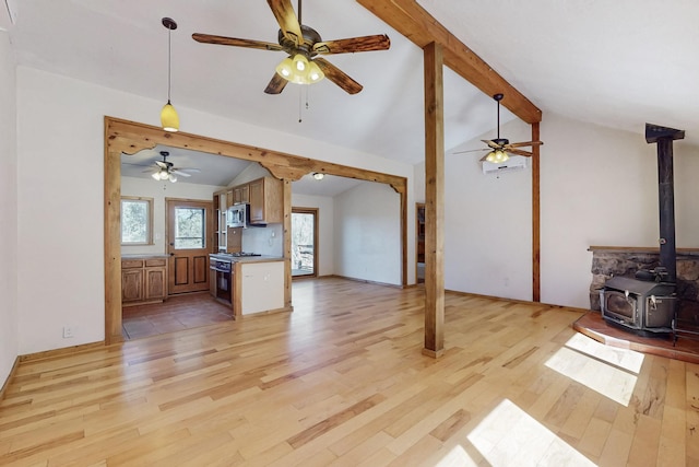 unfurnished living room featuring vaulted ceiling with beams, a wood stove, light wood-type flooring, and ceiling fan