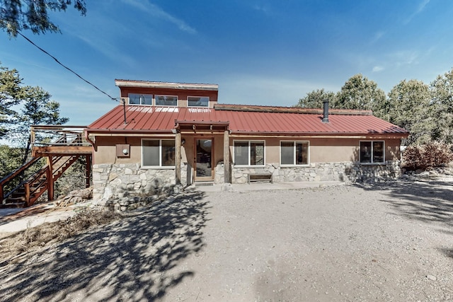 view of front facade with stone siding, stairway, metal roof, and stucco siding