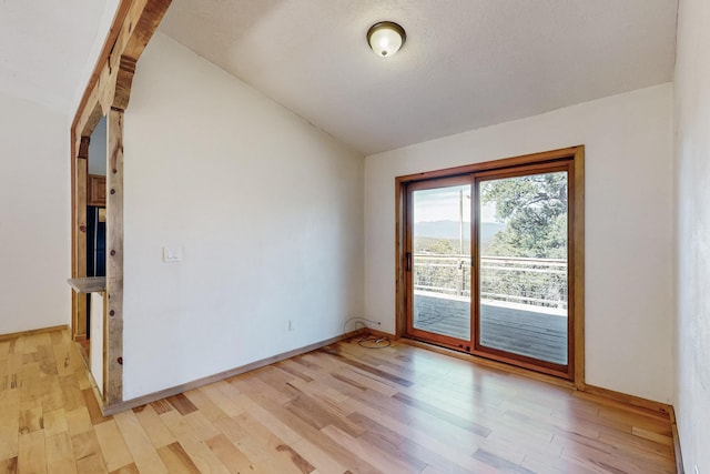 spare room with vaulted ceiling, light wood-style flooring, and baseboards