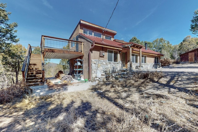 rear view of property with stone siding, stairway, a wooden deck, and stucco siding