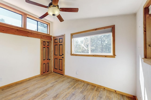 unfurnished room featuring light wood finished floors, plenty of natural light, baseboards, and vaulted ceiling