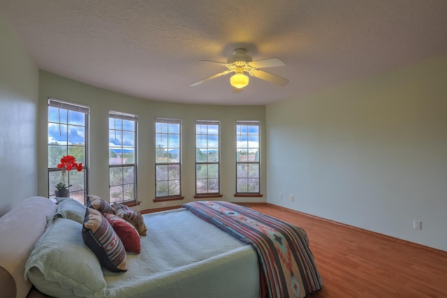 bedroom with ceiling fan, multiple windows, a textured ceiling, and wood finished floors