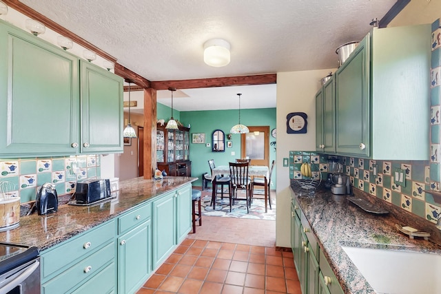 kitchen featuring tasteful backsplash, hanging light fixtures, a sink, a textured ceiling, and green cabinetry