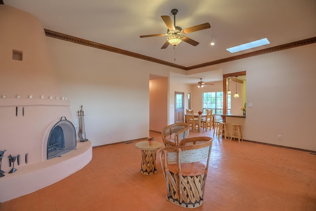 living room with a skylight, baseboards, a fireplace with raised hearth, and crown molding