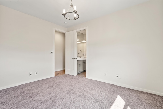 unfurnished bedroom featuring light carpet, ensuite bath, baseboards, and an inviting chandelier