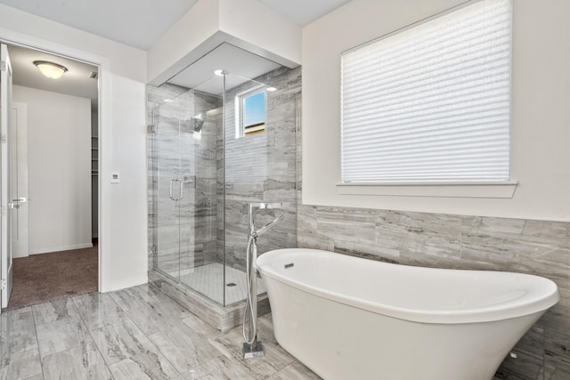 bathroom with a stall shower, a freestanding bath, and tile walls