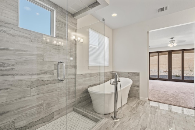 bathroom with visible vents, a ceiling fan, a tile shower, a freestanding tub, and tile walls