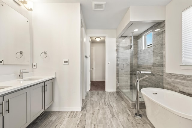 bathroom featuring double vanity, visible vents, a stall shower, a sink, and a freestanding tub