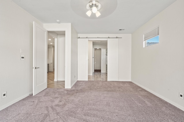 unfurnished bedroom featuring light carpet, visible vents, baseboards, and a barn door