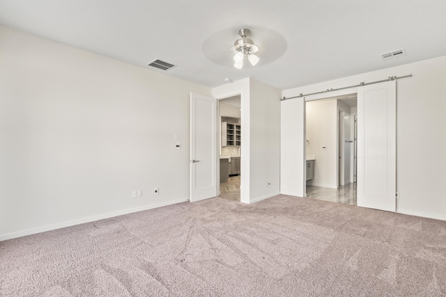 unfurnished bedroom with light carpet, a barn door, visible vents, and connected bathroom