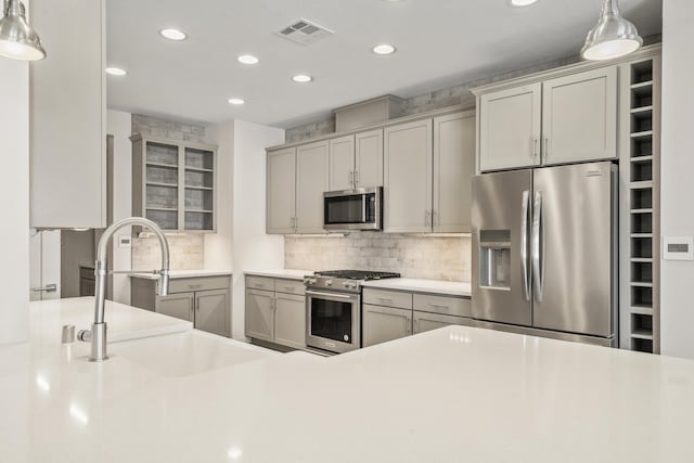 kitchen with pendant lighting, stainless steel appliances, light countertops, visible vents, and a sink