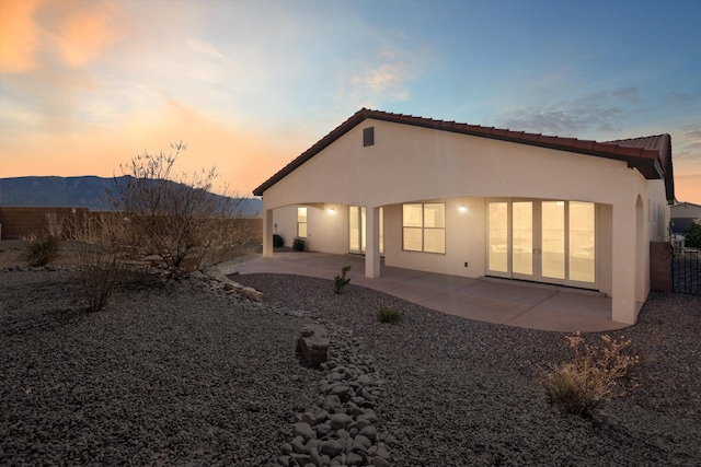 back of property at dusk with a patio, stucco siding, a mountain view, fence, and a tiled roof