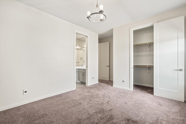 unfurnished bedroom with carpet floors, a closet, ensuite bathroom, an inviting chandelier, and baseboards