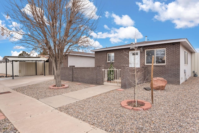 view of front of home with a carport, brick siding, and fence