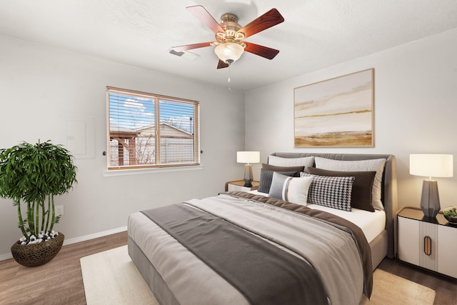 bedroom featuring a ceiling fan, wood finished floors, visible vents, and baseboards