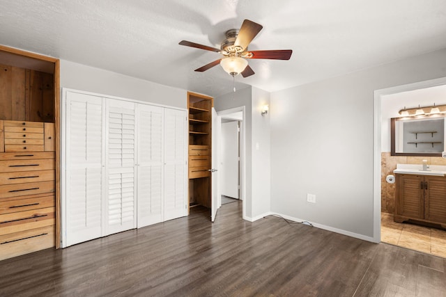 unfurnished bedroom with baseboards, a ceiling fan, connected bathroom, dark wood-type flooring, and a closet