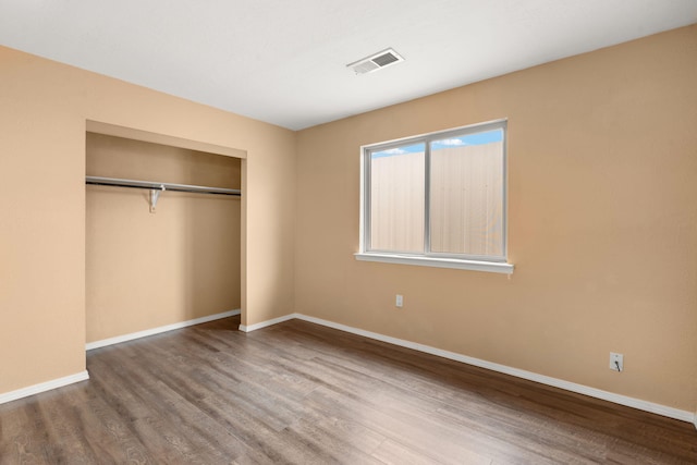 unfurnished bedroom with baseboards, a closet, visible vents, and wood finished floors