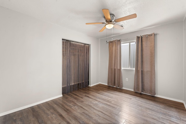 empty room featuring a textured ceiling, wood finished floors, a ceiling fan, and baseboards