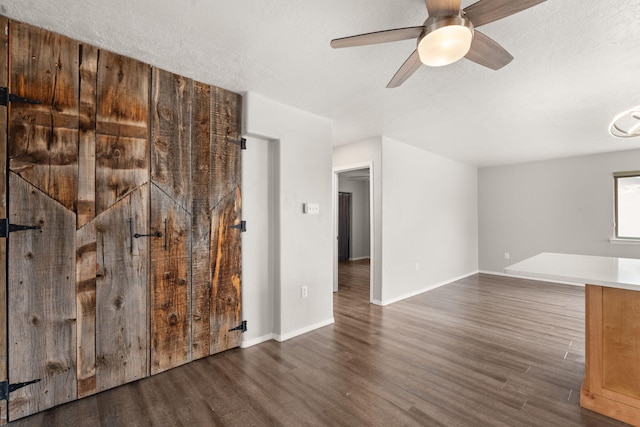 spare room with ceiling fan, a textured ceiling, baseboards, and dark wood-type flooring