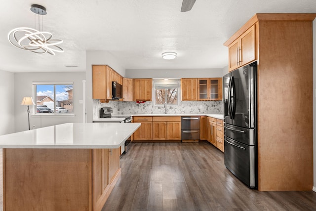 kitchen featuring decorative light fixtures, stainless steel appliances, light countertops, glass insert cabinets, and dark wood-type flooring