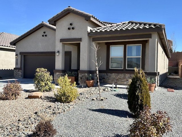 mediterranean / spanish house with driveway, stone siding, a tiled roof, an attached garage, and stucco siding