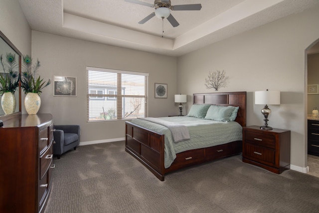 bedroom with ceiling fan, baseboards, a tray ceiling, and dark colored carpet