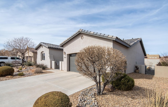 exterior space featuring a tile roof, stucco siding, a gate, a garage, and driveway