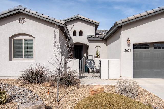 property entrance with a garage, a tile roof, a gate, fence, and stucco siding