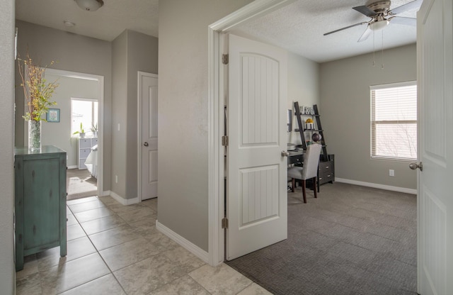 corridor with light carpet, light tile patterned floors, baseboards, and a textured ceiling