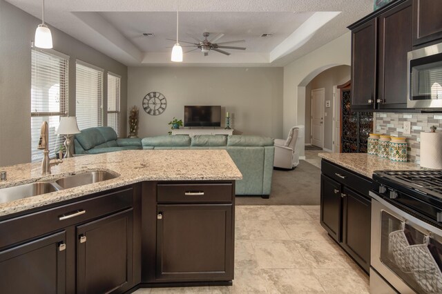 kitchen with arched walkways, open floor plan, a tray ceiling, stainless steel appliances, and a sink