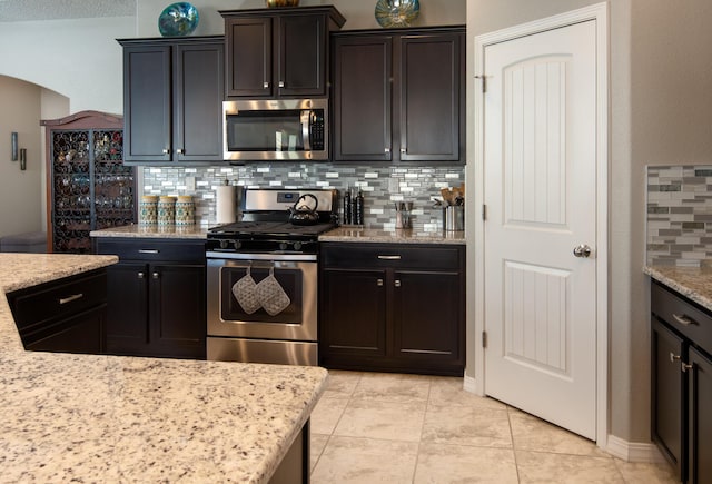 kitchen with light tile patterned floors, stainless steel appliances, light stone counters, and backsplash