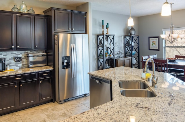 kitchen featuring tasteful backsplash, appliances with stainless steel finishes, hanging light fixtures, light stone countertops, and a sink