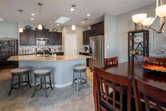 kitchen featuring stainless steel appliances, a skylight, a kitchen breakfast bar, light stone countertops, and an island with sink