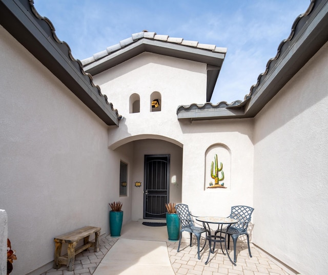 doorway to property featuring a patio area, a tiled roof, and stucco siding