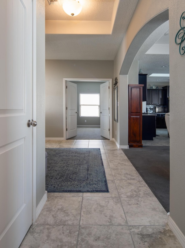 corridor with light tile patterned floors, baseboards, visible vents, arched walkways, and a textured ceiling