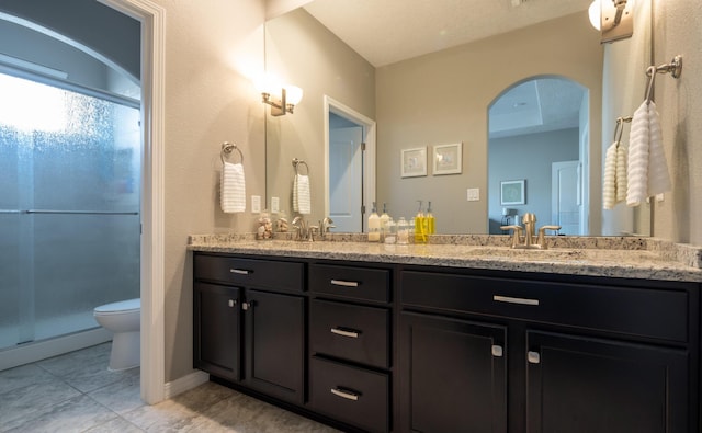 bathroom featuring toilet, a stall shower, double vanity, and a sink