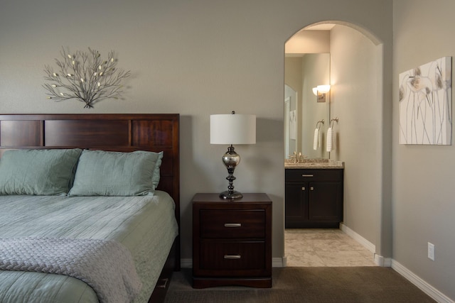 bedroom with arched walkways, ensuite bathroom, light colored carpet, a sink, and baseboards