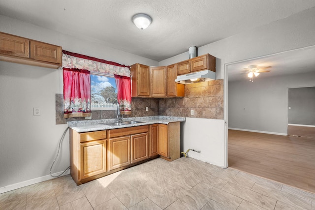 kitchen with tasteful backsplash, brown cabinets, light countertops, under cabinet range hood, and a sink