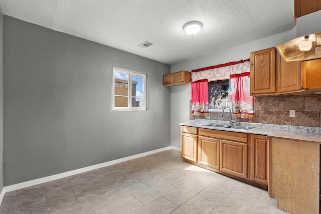 kitchen with a sink, visible vents, a healthy amount of sunlight, brown cabinets, and decorative backsplash