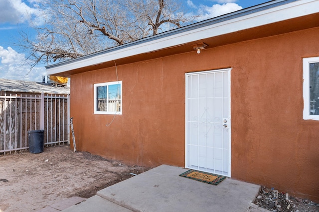 entrance to property featuring fence, a patio, and stucco siding