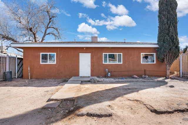 view of front facade featuring a chimney, fence, and stucco siding